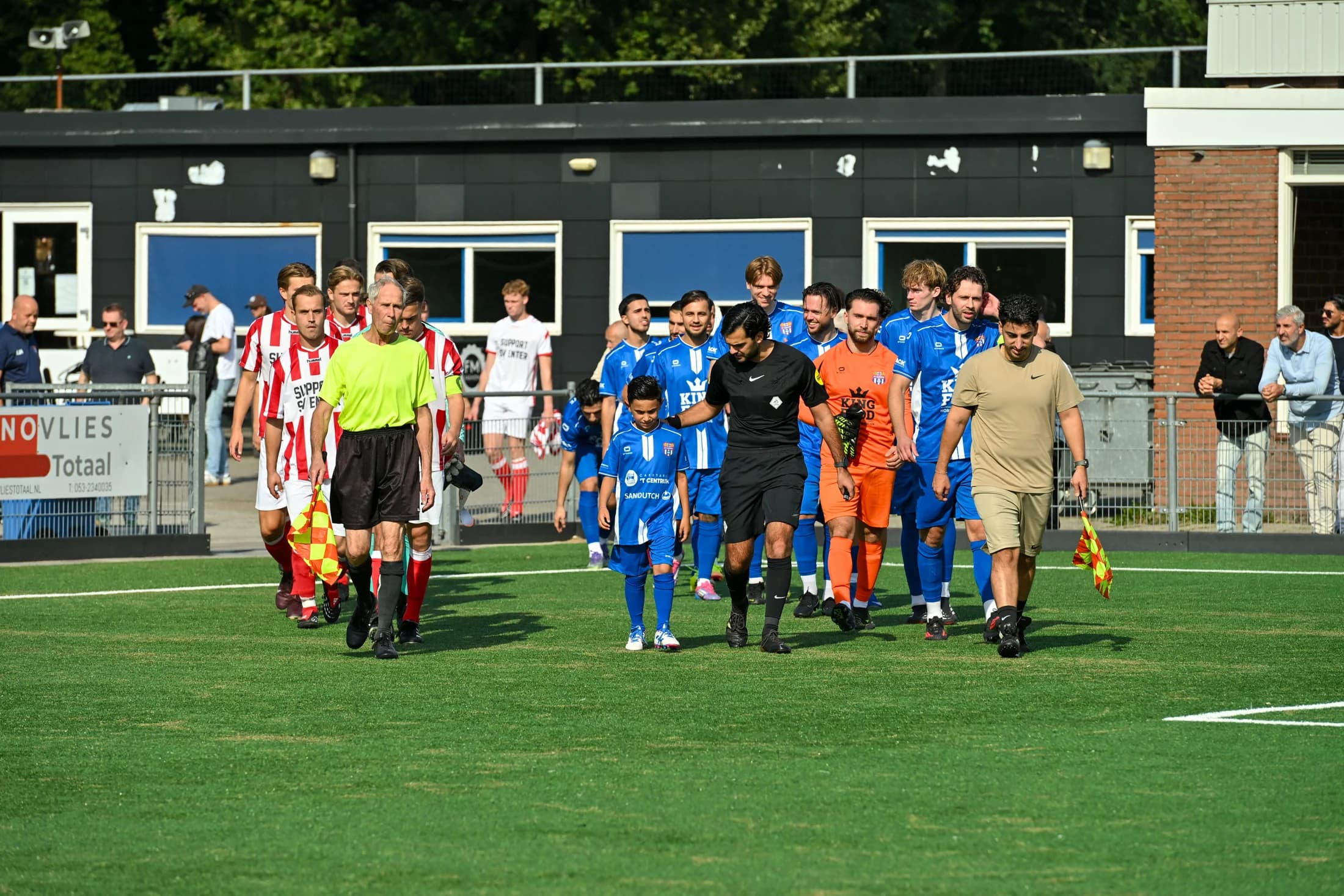 Spelers, jeugdleden en scheidsrechters betreden het veld